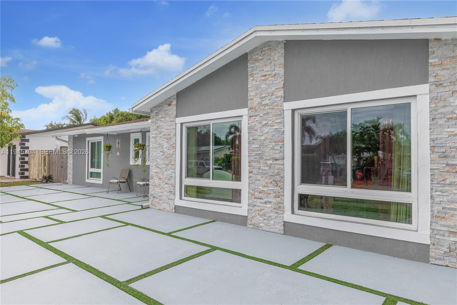 A gray house exterior features stone accents, large windows, and a concrete paver patio — 15244 SW 108th Ct, Miami FL 33157, MIAMI, FL