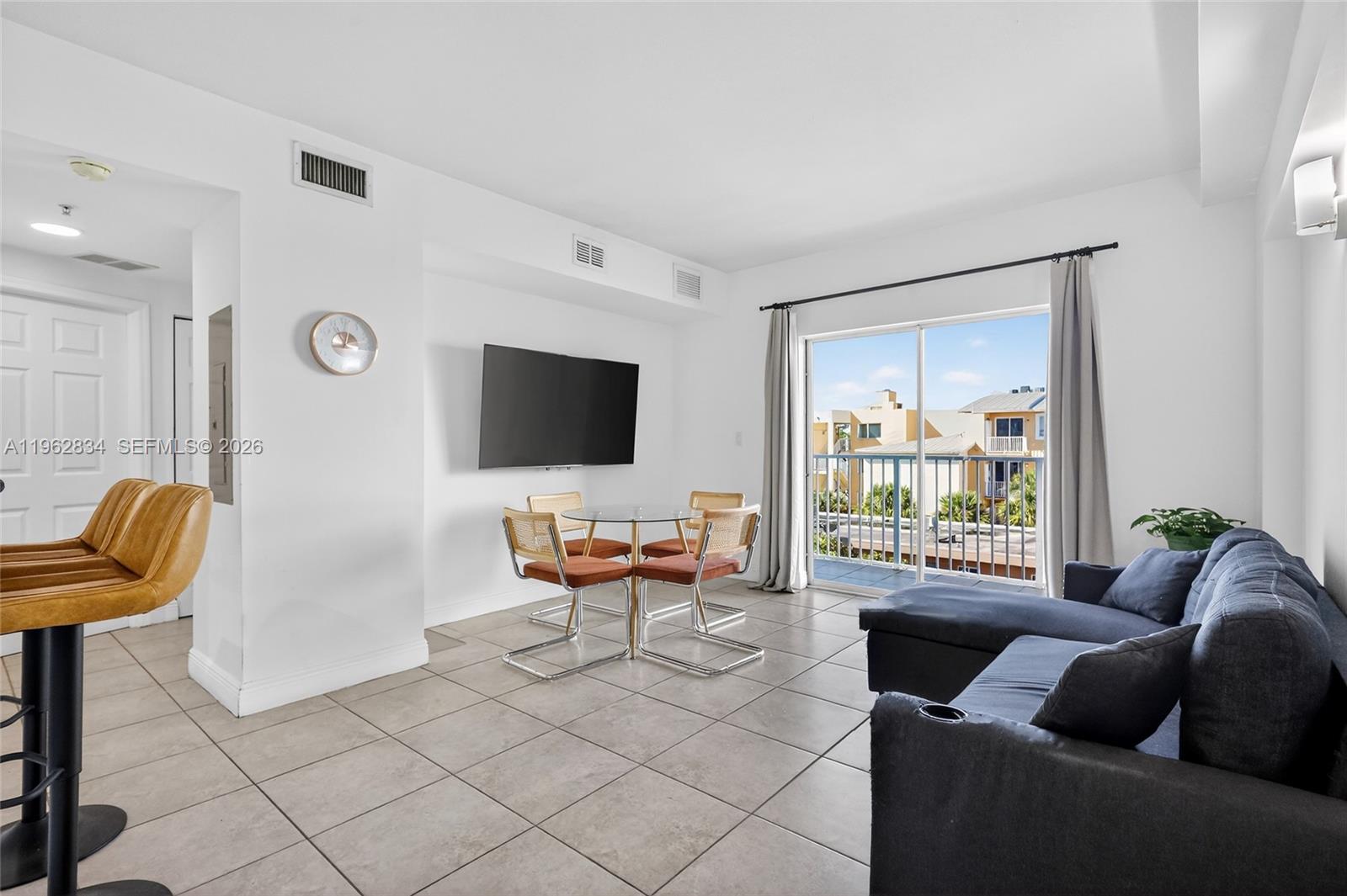 A living room features tile flooring, a dining set, a wall-mounted television, and a balcony — 134 SW 7th Ave # 404, Miami FL 33130, MIAMI, FL