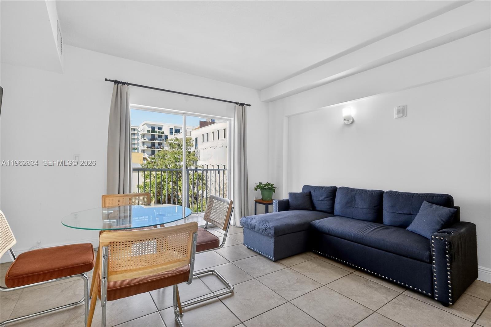 A living and dining area features a blue sectional sofa, glass table, and balcony access — 134 SW 7th Ave # 404, Miami FL 33130, MIAMI, FL