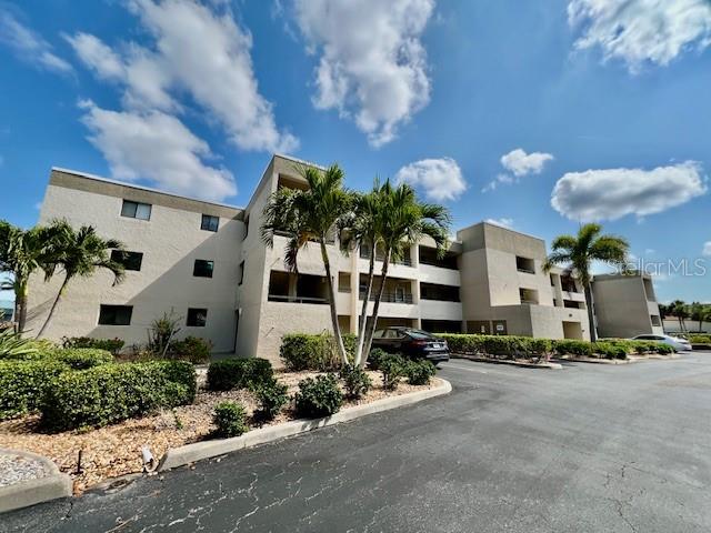 A multi-story apartment building with beige stucco walls and palm trees in the foreground — 801 ISLAMORADA BOULEVARD UNIT 26C, PUNTA GORDA, FL