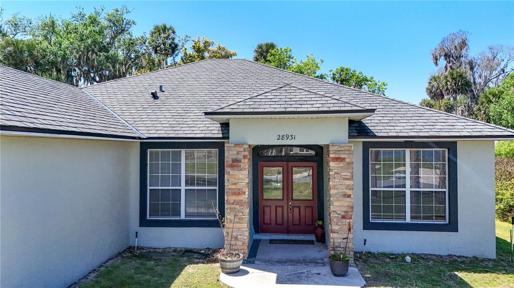 A single-story house exterior features a stone-accented entryway with double doors and gray siding — 28931 BEAUCLAIRE DRIVE, TAVARES, FL