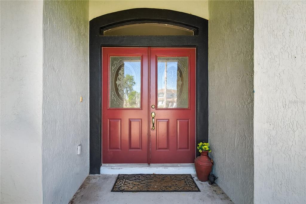 A red double front door with glass inserts is set within a black arched frame — 28931 BEAUCLAIRE DRIVE, TAVARES, FL