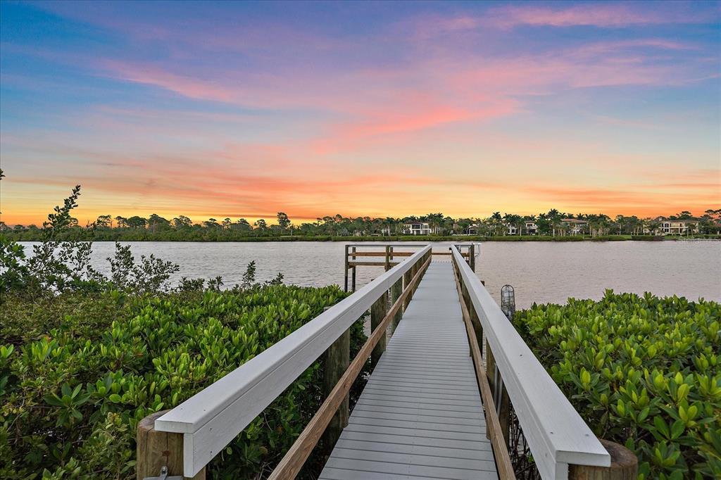 A wooden pier extends over water toward a distant shoreline under a sunset sky — 756 N MANASOTA KEY ROAD, ENGLEWOOD, FL