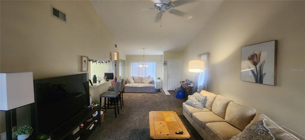 A living room features a beige sofa, a television, a breakfast bar, and carpeted flooring — 2229 PARKLAKE POINT UNIT G7, VENICE, FL