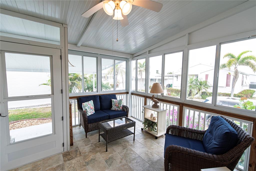 A sunroom features tiled flooring, wicker furniture, and large windows overlooking a residential neighborhood — 22 BELCHER DRIVE, PUNTA GORDA, FL