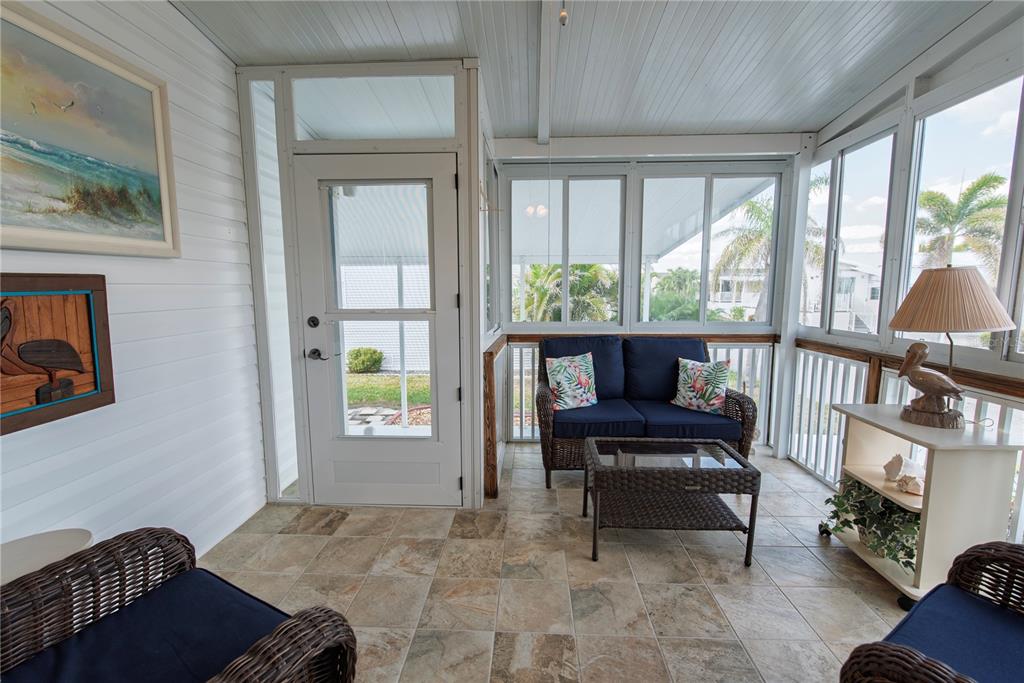 A sunroom features tiled floors, wicker furniture, a screen door, and large windows overlooking palm trees — 22 BELCHER DRIVE, PUNTA GORDA, FL
