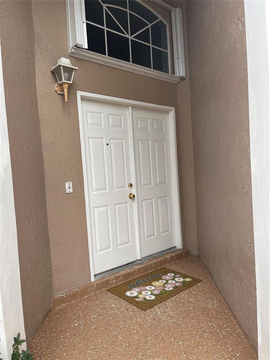A white double front door with a floral welcome mat sits in a recessed entryway — 480 Somerset Way, Weston FL 33326, WESTON, FL