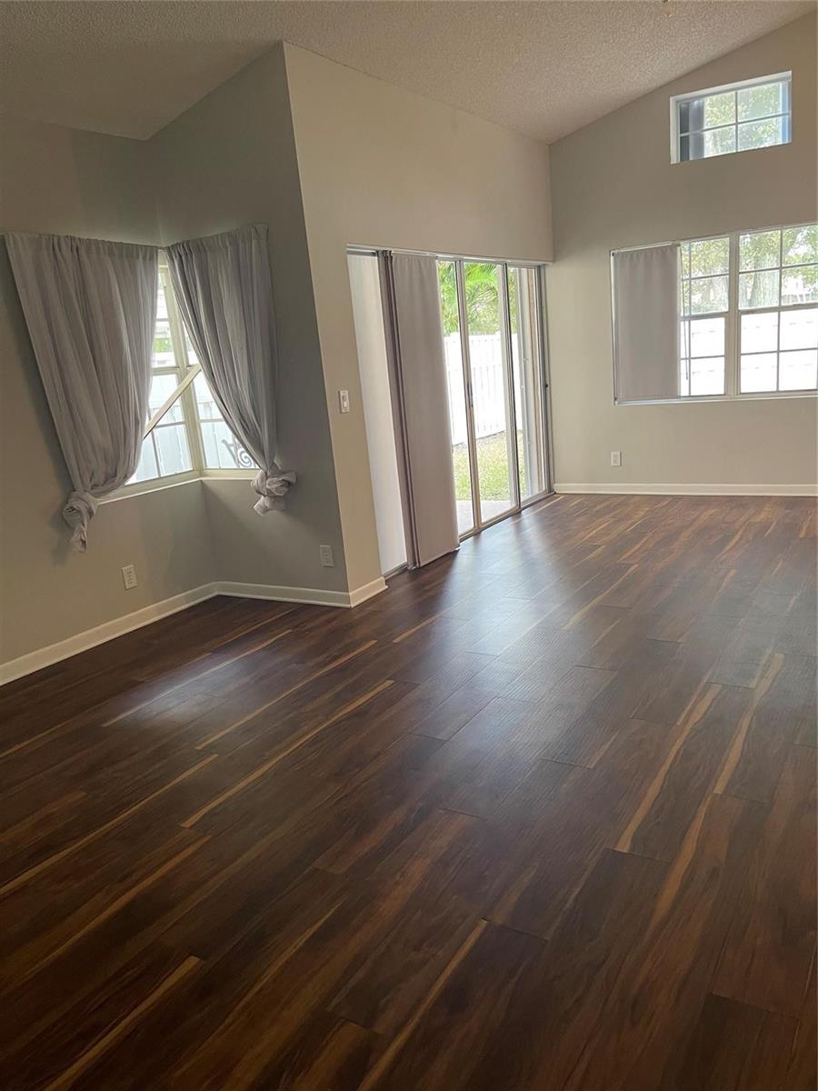 A living room with dark wood-look flooring, large windows, and a sliding glass door — 480 Somerset Way, Weston FL 33326, WESTON, FL