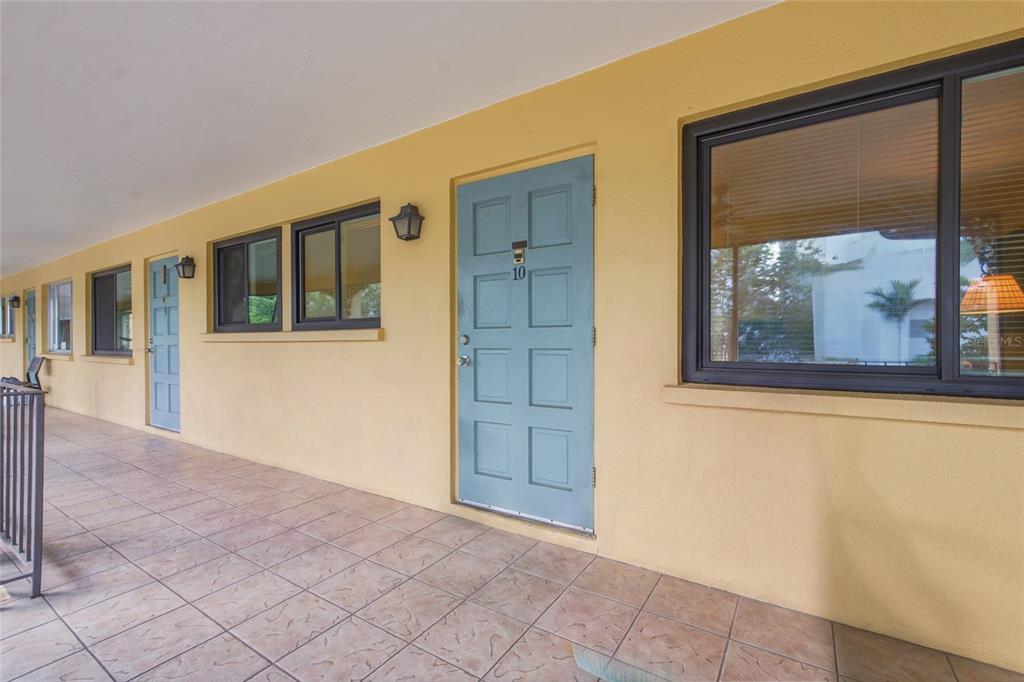 A covered outdoor walkway with tiled flooring leads to blue doors and windows on a building — 615 S PALM AVENUE UNIT 10, SARASOTA, FL
