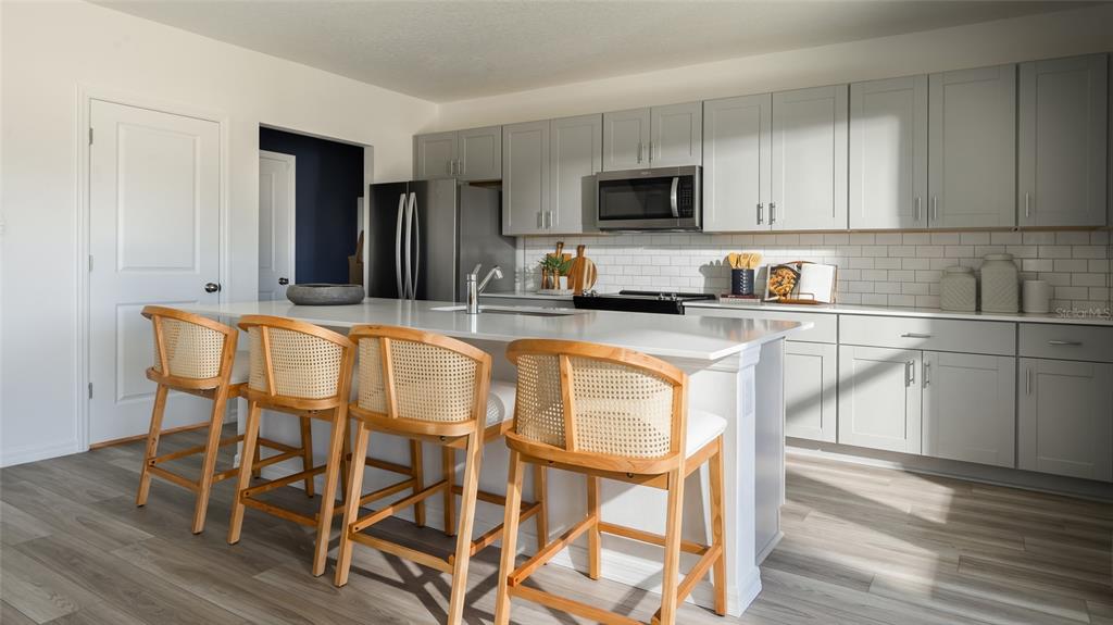 A modern kitchen features a large white island with four cane-back stools and gray cabinetry — 31691 OYSTER TRELLIS LANE, WESLEY CHAPEL, FL