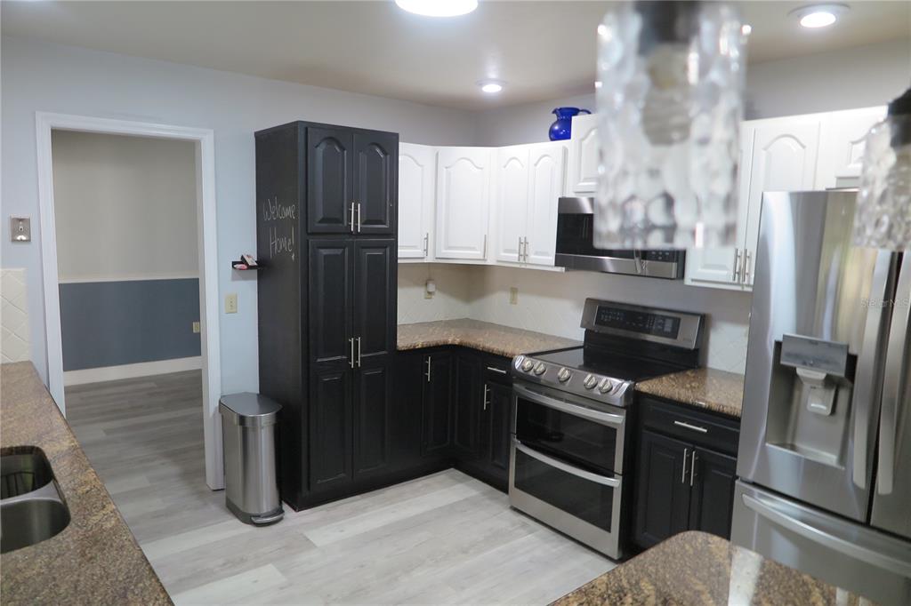 A kitchen features two-toned black and white cabinets, granite countertops, and stainless steel appliances — 8215 SW 47TH ROAD, GAINESVILLE, FL