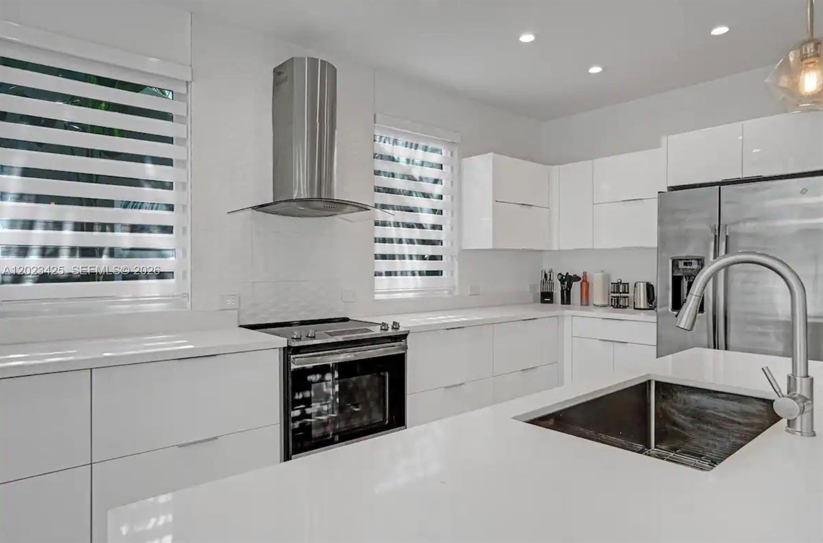 A modern white kitchen features stainless steel appliances, a range hood, and a center island — 1547 Jackson St, Hollywood FL 33020, HOLLYWOOD, FL