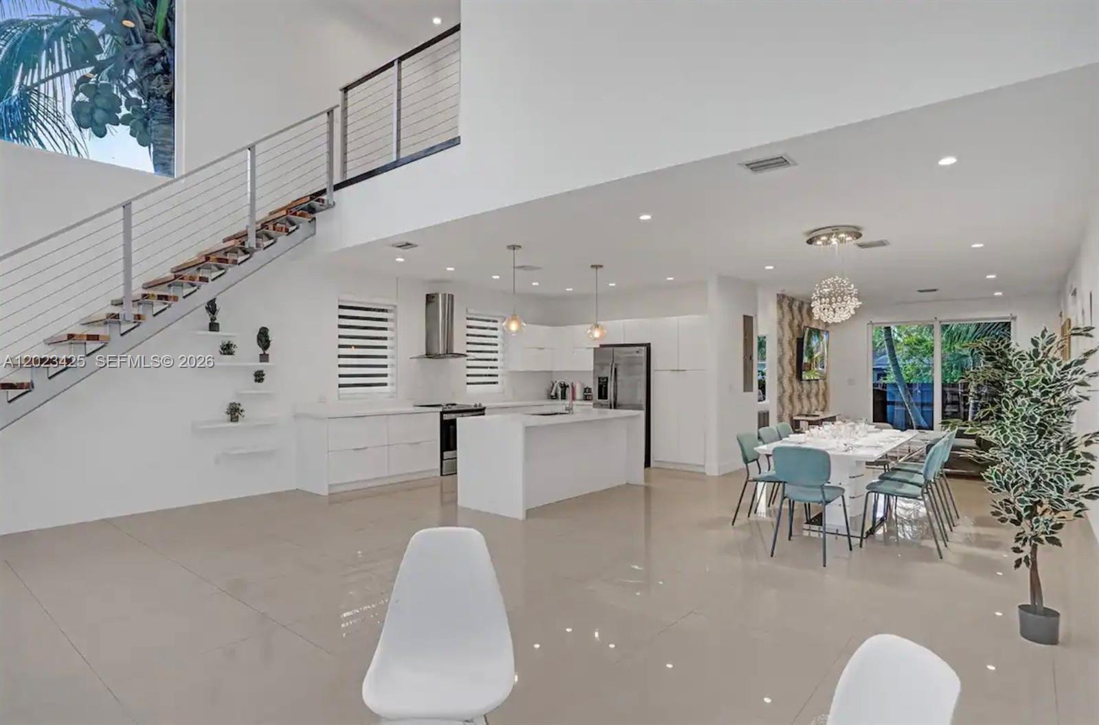 A modern open-concept kitchen and dining area features white cabinetry, tile flooring, and a staircase — 1547 Jackson St, Hollywood FL 33020, HOLLYWOOD, FL