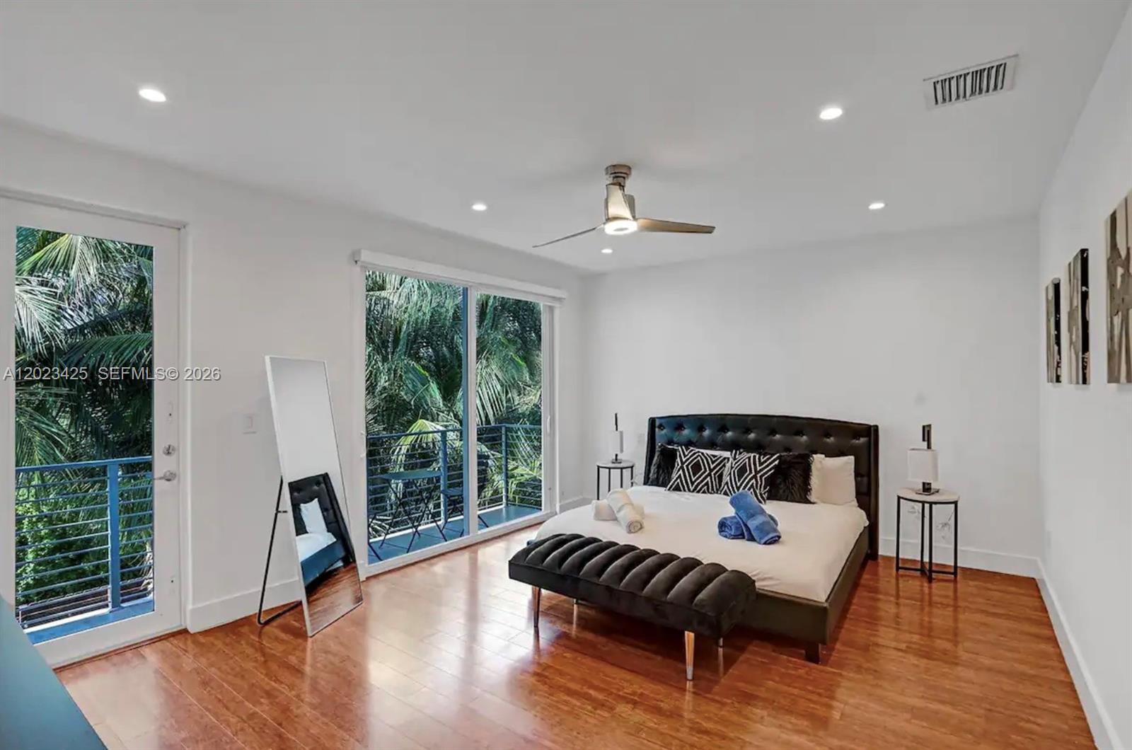 A bedroom with a tufted black bed, hardwood floors, and a balcony with palm trees — 1547 Jackson St, Hollywood FL 33020, HOLLYWOOD, FL