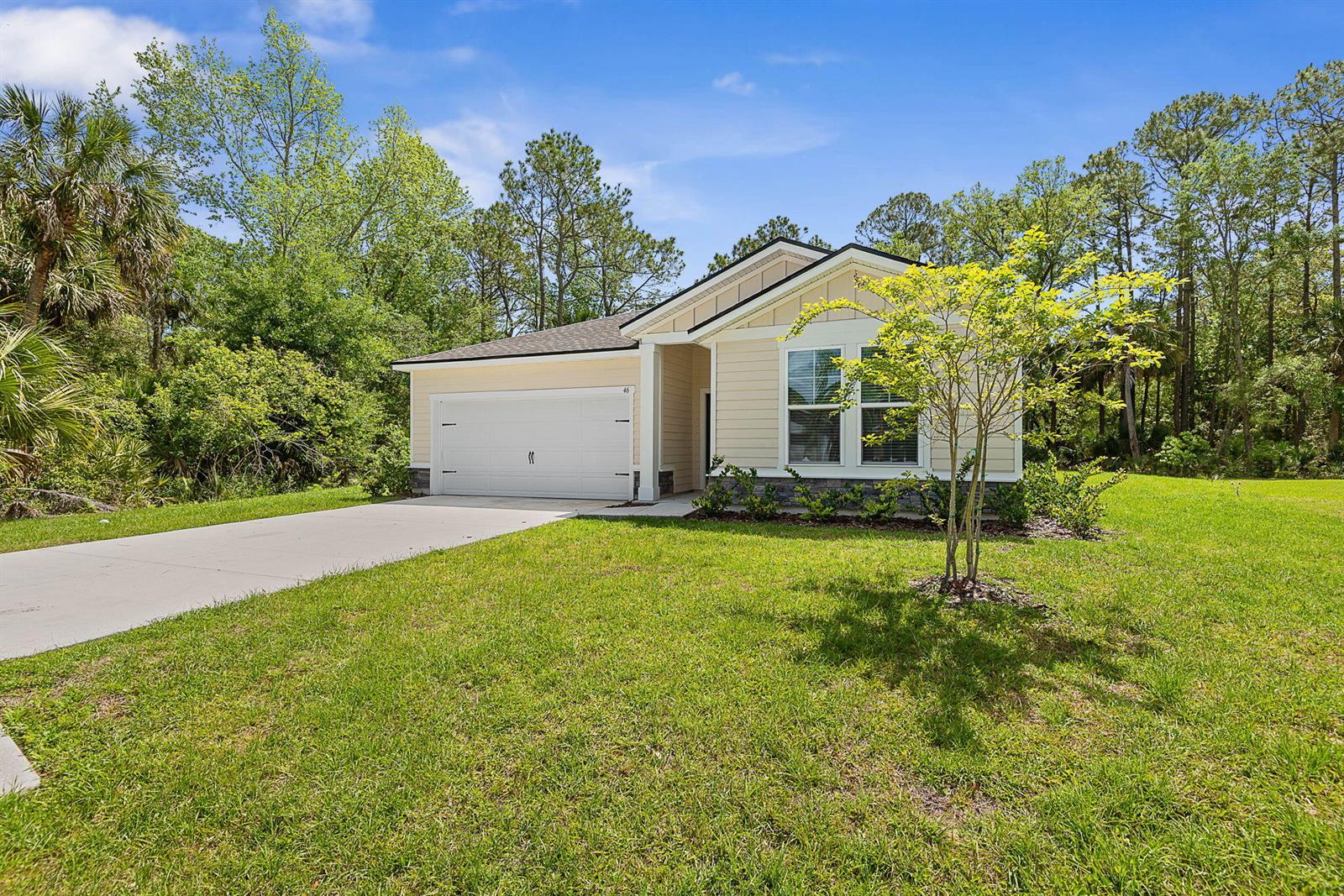 A single-story house with beige siding, a white garage door, and a grassy front yard — 46 Poplar Drive, Palm Coast FL 32164, PALM COAST, FL