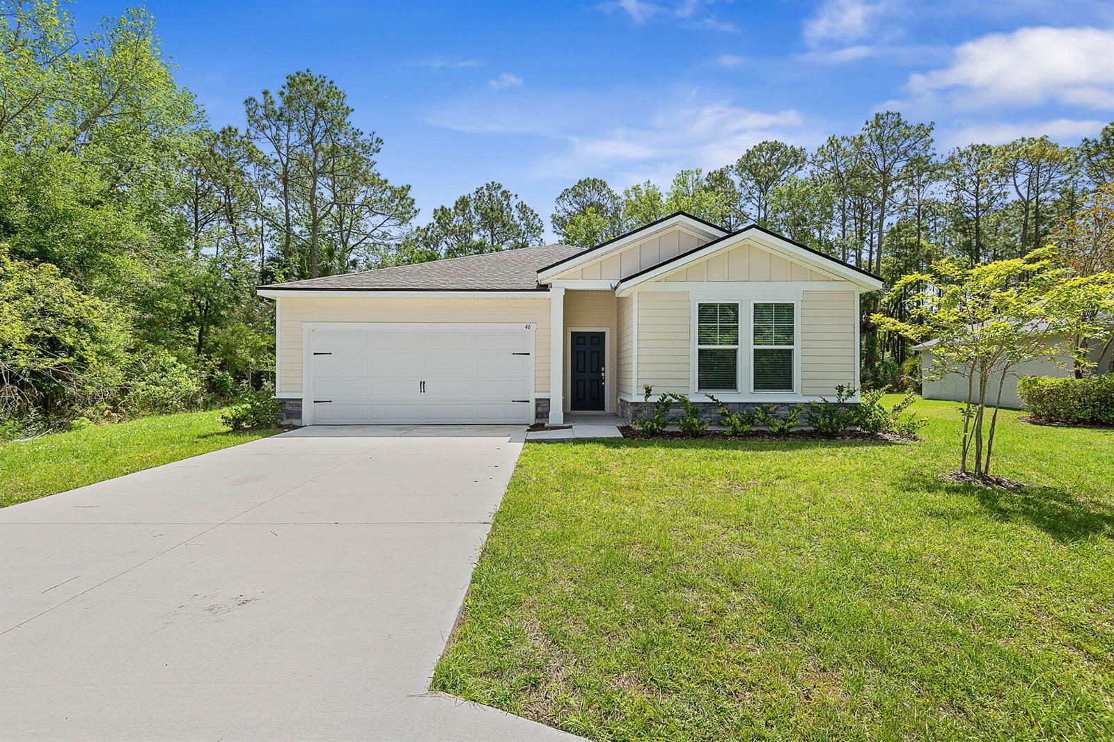 A single-story house with light yellow siding, a white garage door, and a front porch — 46 Poplar Drive, Palm Coast FL 32164, PALM COAST, FL