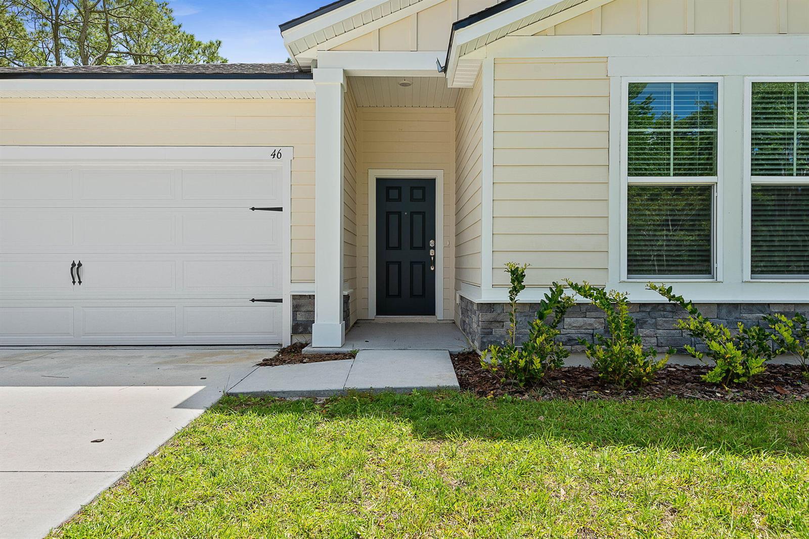 The exterior of a house features light yellow siding, a dark front door, and stone accents — 46 Poplar Drive, Palm Coast FL 32164, PALM COAST, FL