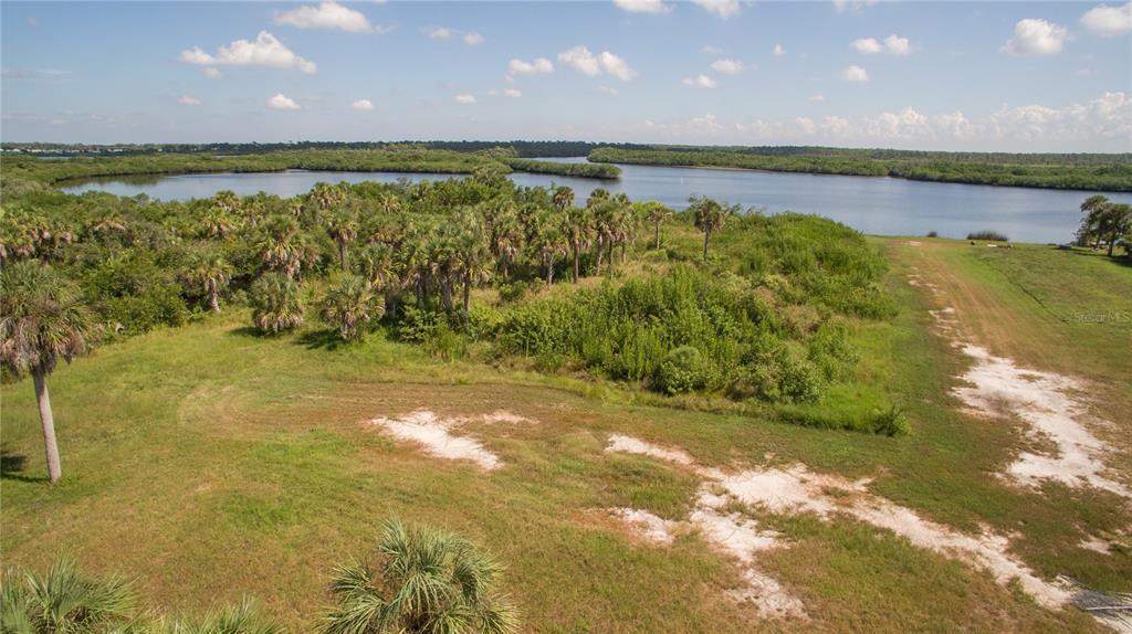 An aerial view shows a grassy lot with palm trees bordering a large body of water — DEER COURT, VENICE, FL