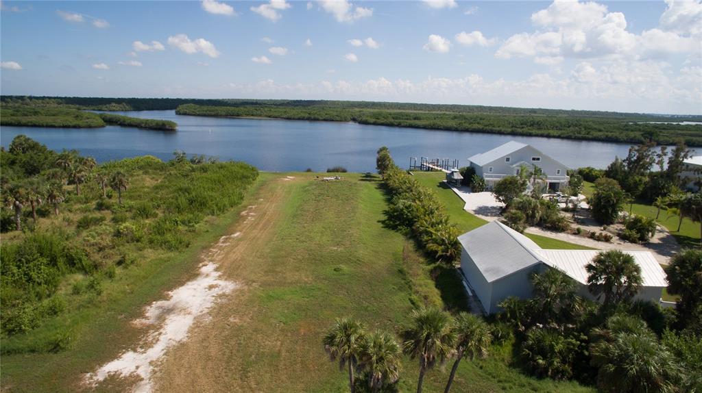 An aerial view shows a vacant grassy lot next to a waterfront house and dock — DEER COURT, VENICE, FL