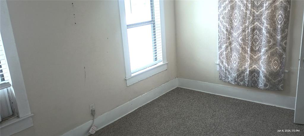 An empty bedroom features beige walls, gray carpeting, two windows with blinds, and patterned curtains — 108 MURRAY WAY UNIT 1, SOUTH DAYTONA, FL