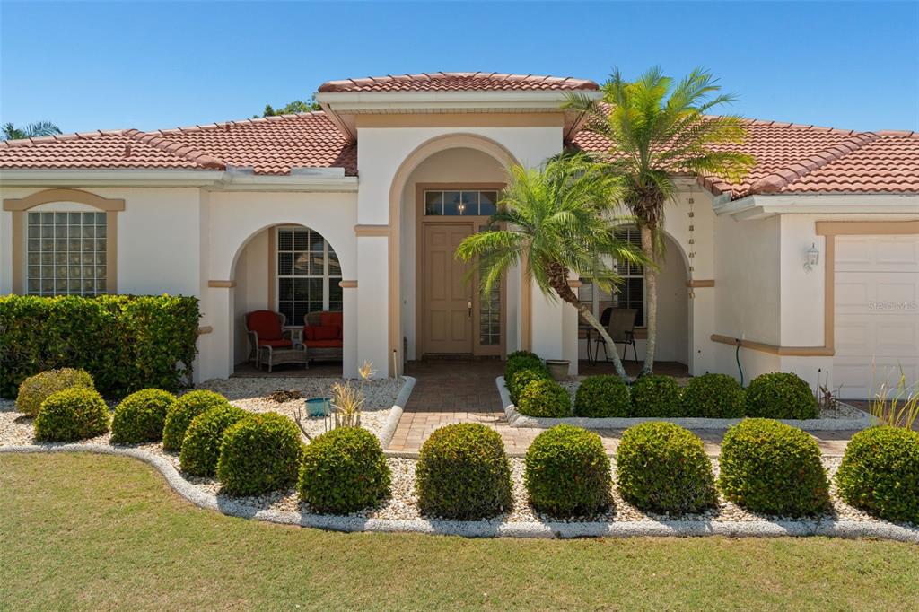 The exterior of a single-story home features a tiled roof, arched entryway, and landscaped garden — 1134 SIGNATURE DRIVE, SUN CITY CENTER, FL