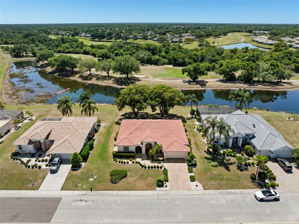 An aerial view shows three houses along a street with a pond and golf course behind — 1134 SIGNATURE DRIVE, SUN CITY CENTER, FL