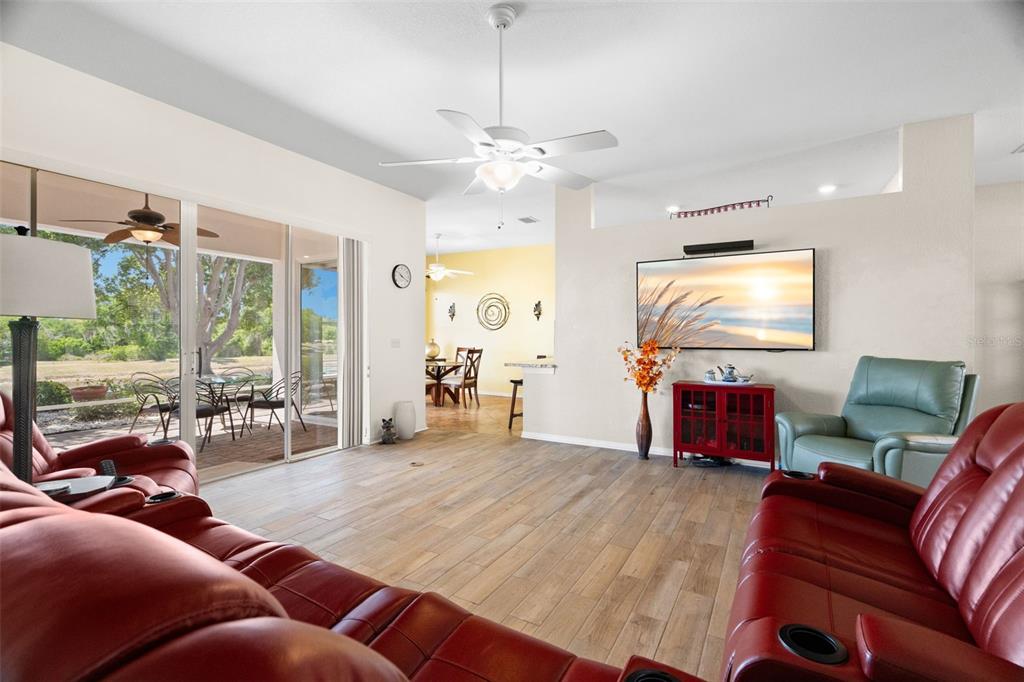 A living room features red leather sofas, a television, and sliding glass doors to a patio — 1134 SIGNATURE DRIVE, SUN CITY CENTER, FL