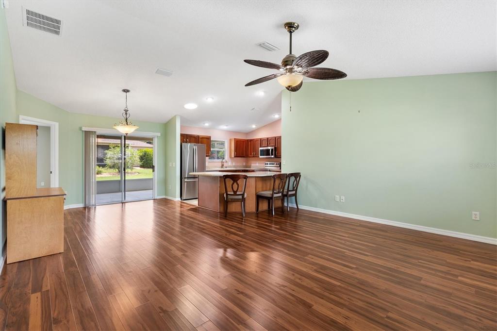 An open-concept living area features wood flooring, a kitchen island, and sliding glass patio doors — 1630 ABERCROMBIE WAY, THE VILLAGES, FL