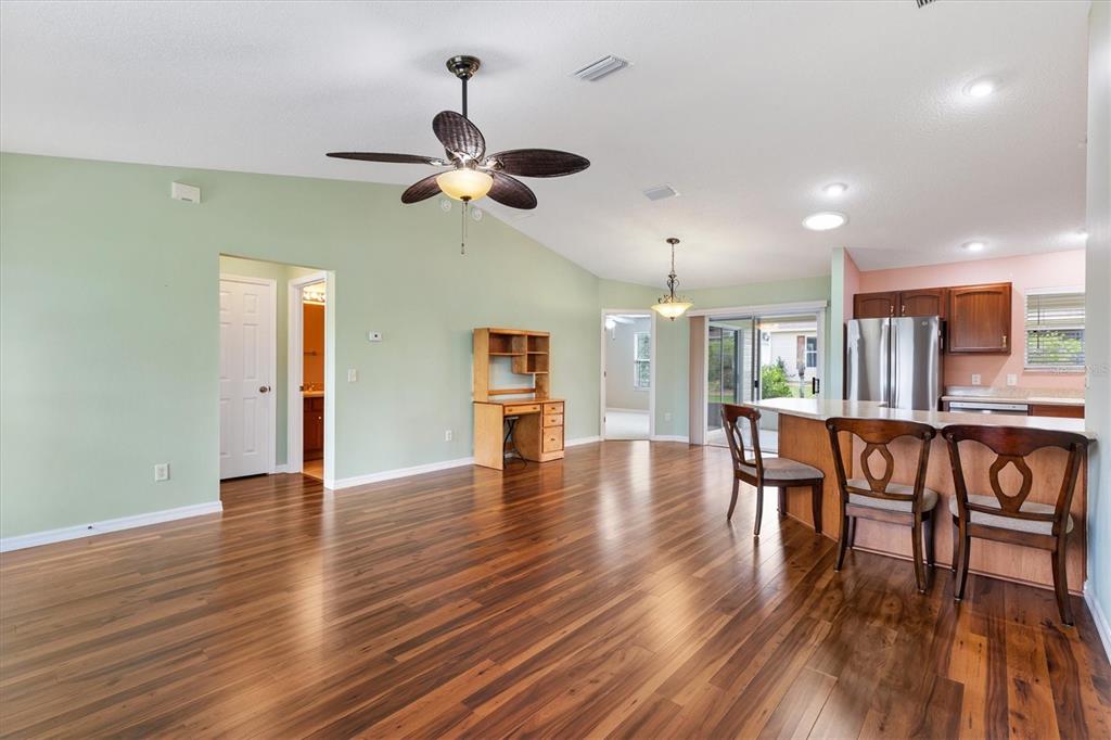 A living room with wood flooring, a ceiling fan, and an open kitchen with bar seating — 1630 ABERCROMBIE WAY, THE VILLAGES, FL