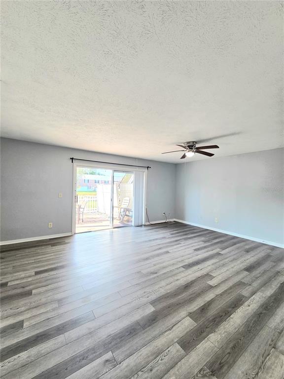 An empty living room features light gray walls, wood-look flooring, a ceiling fan, and sliding doors — 13690 ORANGE SUNSET DRIVE UNIT 102, TAMPA, FL