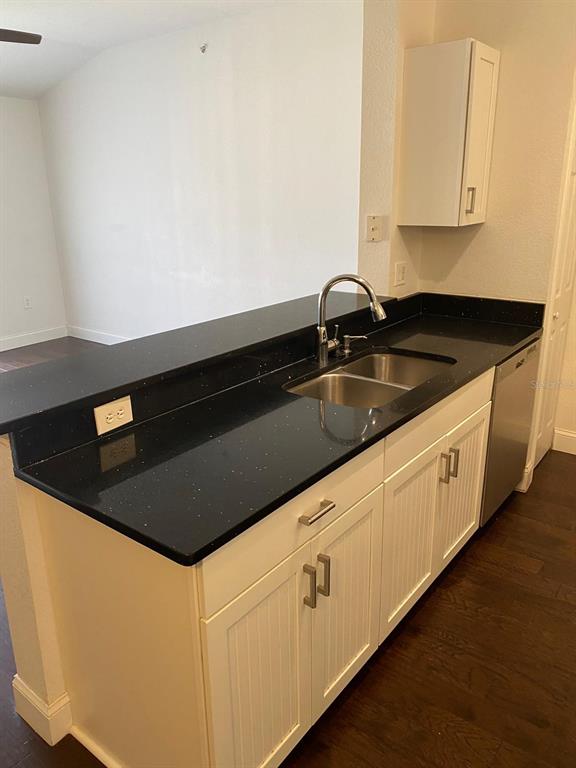 A kitchen features dark countertops, white cabinetry, stainless steel appliances, and dark wood flooring — 5475 VINELAND ROAD UNIT 8311, ORLANDO, FL
