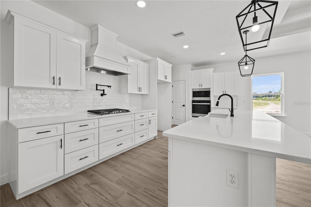 A modern white kitchen features quartz countertops, stainless steel appliances, and wood-look tile flooring — 1050 SW 67TH WAY, GAINESVILLE, FL