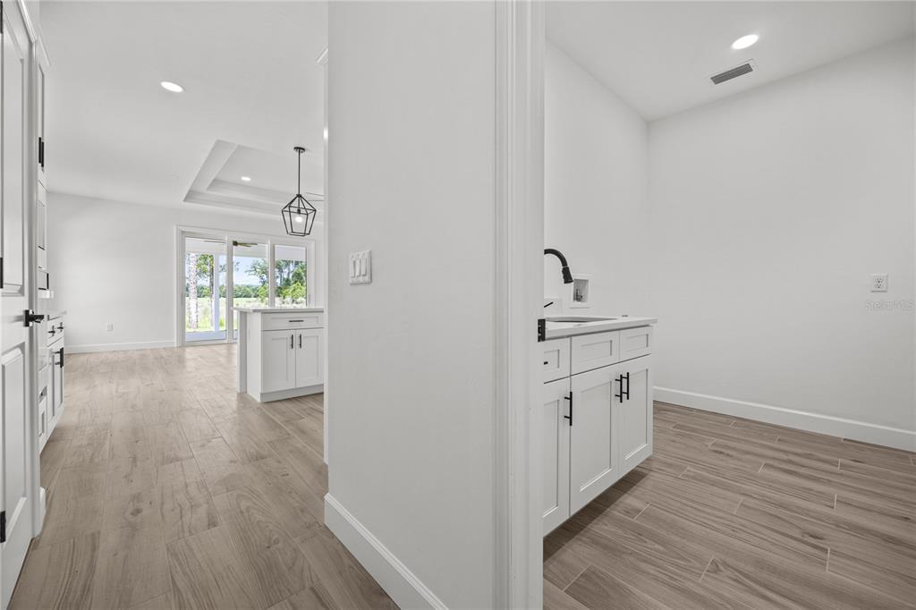 A laundry room with white cabinets and a sink opens into a bright, modern kitchen — 1050 SW 67TH WAY, GAINESVILLE, FL