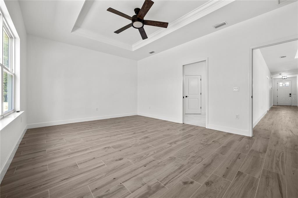 A bright, empty room features light wood-look tile flooring, a tray ceiling, and a ceiling fan — 1050 SW 67TH WAY, GAINESVILLE, FL