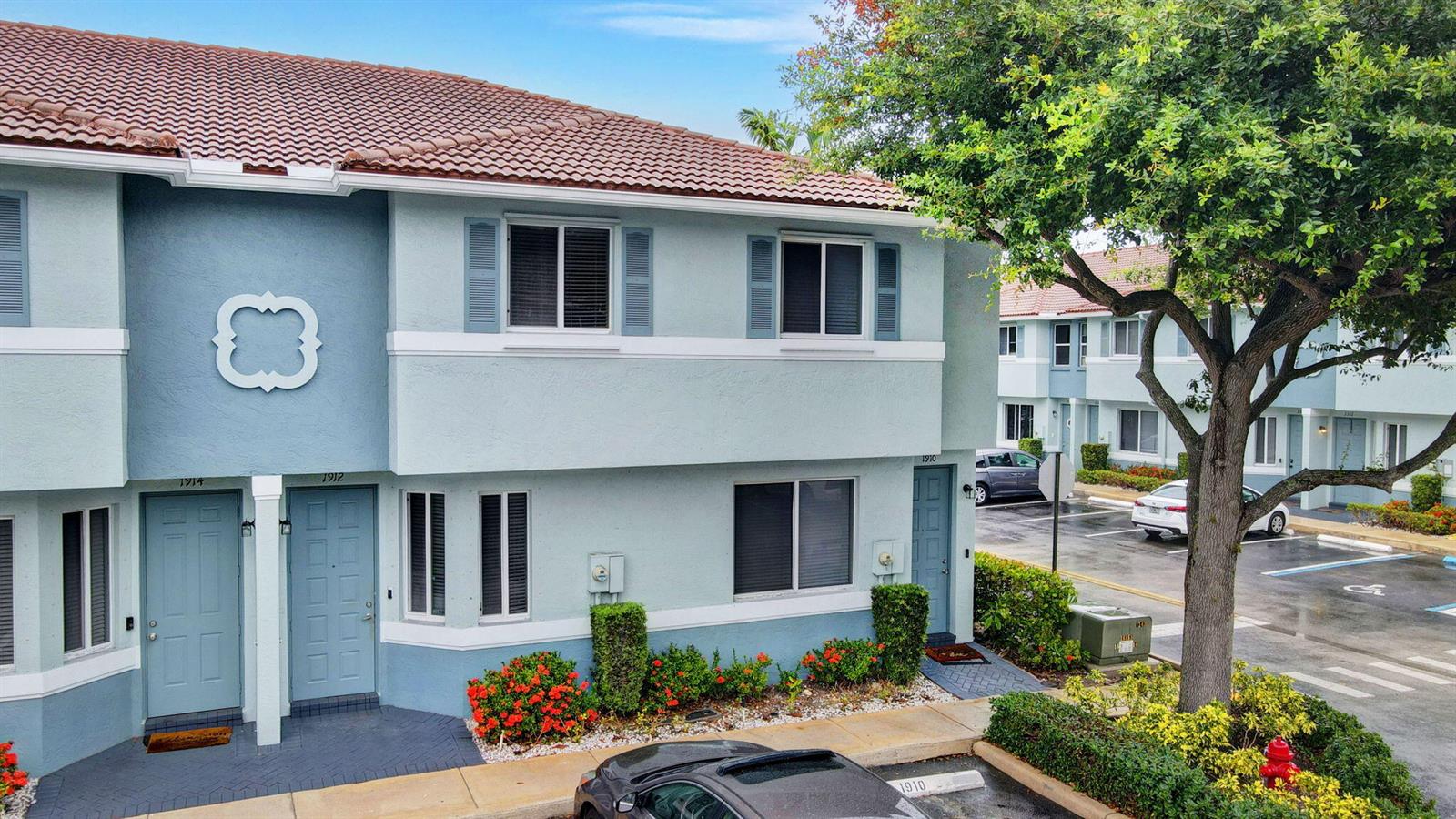 A two-story blue townhouse exterior features a tiled roof, shuttered windows, and a parking lot — 1912 Hibiscus Lane, Riviera Beach FL 33404, RIVIERA BEACH, FL