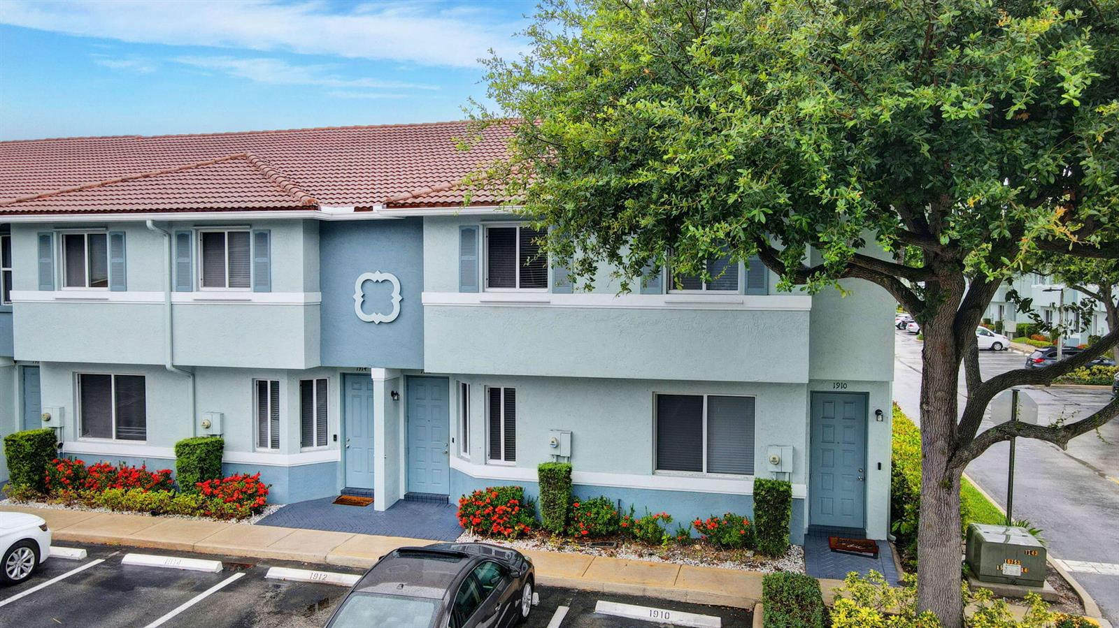 A two-story townhouse exterior features light blue stucco walls, a tiled roof, and parking spaces — 1912 Hibiscus Lane, Riviera Beach FL 33404, RIVIERA BEACH, FL
