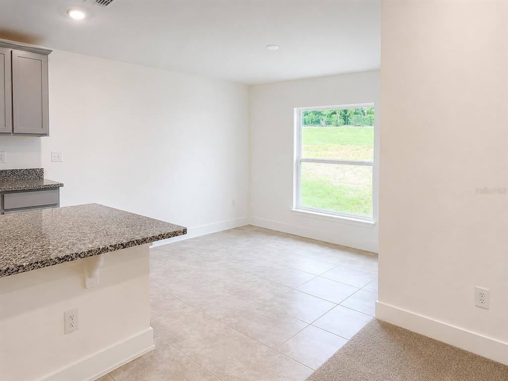 A kitchen with granite countertops and gray cabinets opens to a tiled dining area — 259 VERNY GROVE LANE, LEESBURG, FL