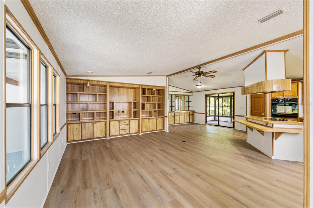 A living room with wood-look flooring, built-in shelving, and an open kitchen with a bar — 1004 ANN AVENUE, LADY LAKE, FL