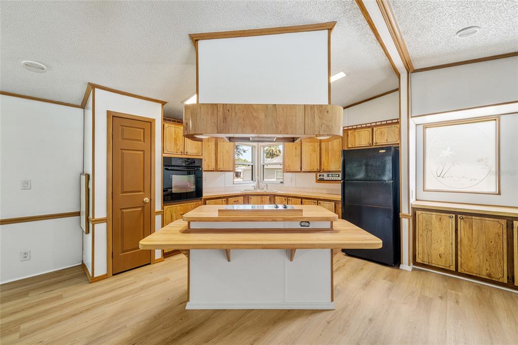 A kitchen features a central island with a cooktop, wood cabinetry, and light wood flooring — 1004 ANN AVENUE, LADY LAKE, FL