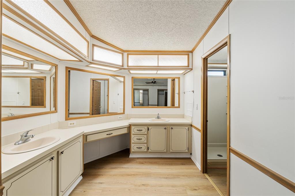 A bathroom with dual sinks, a vanity area, wood-look flooring, and large wall mirrors — 1004 ANN AVENUE, LADY LAKE, FL