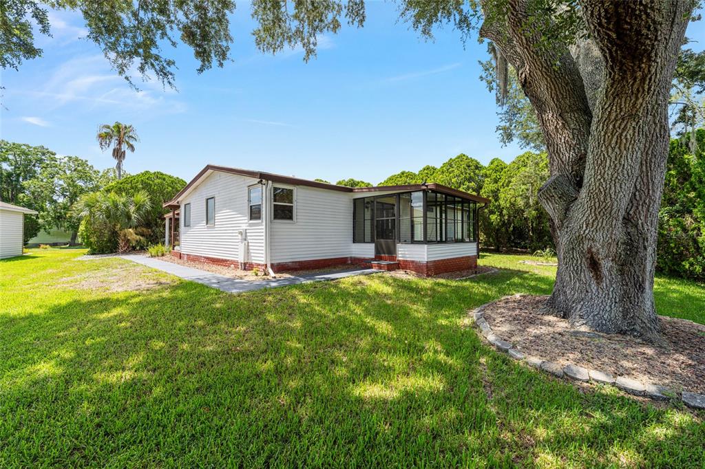 A white single-story house with a screened-in porch sits on a grassy lawn near trees — 1004 ANN AVENUE, LADY LAKE, FL
