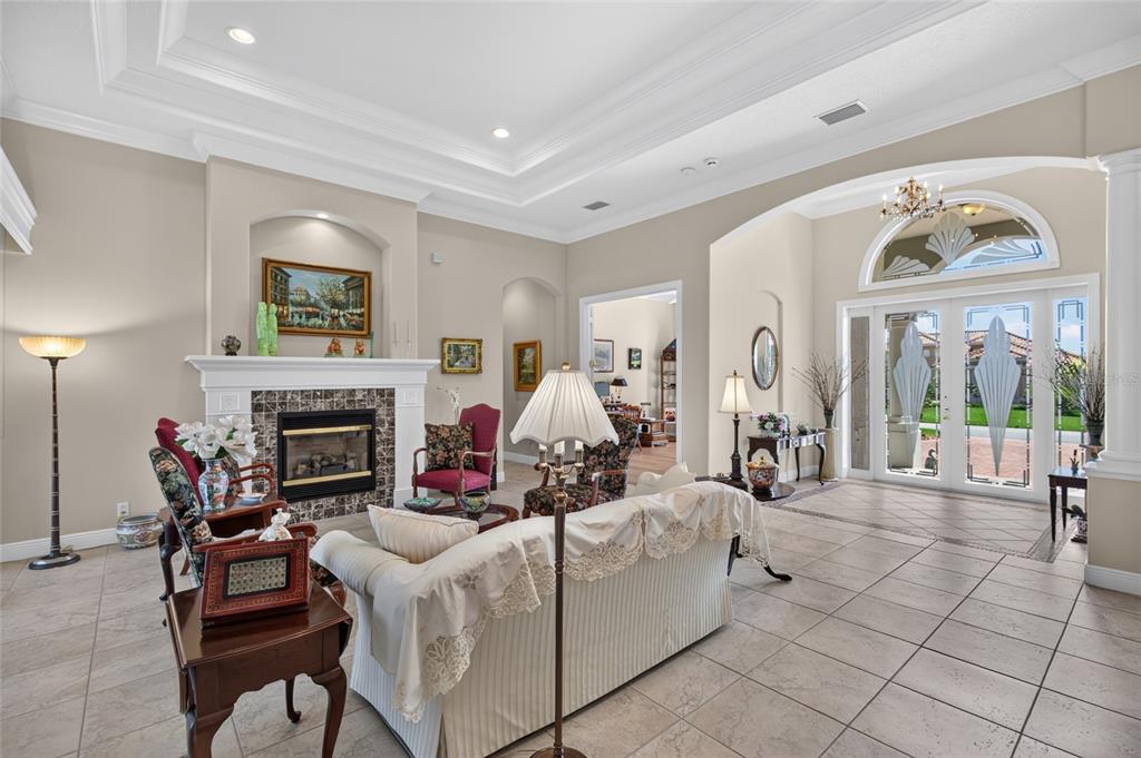 A living room features a fireplace, tile flooring, tray ceilings, and glass-paneled double entry doors — 32 SAN GABRIEL LANE, PALM COAST, FL