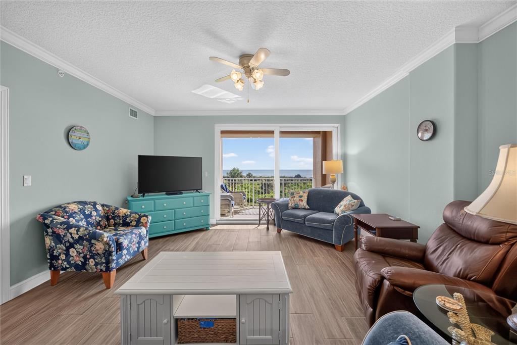 A living room features a floral armchair, blue sofa, brown leather recliner, and ocean view balcony — 60 SURFVIEW DRIVE UNIT 206, PALM COAST, FL