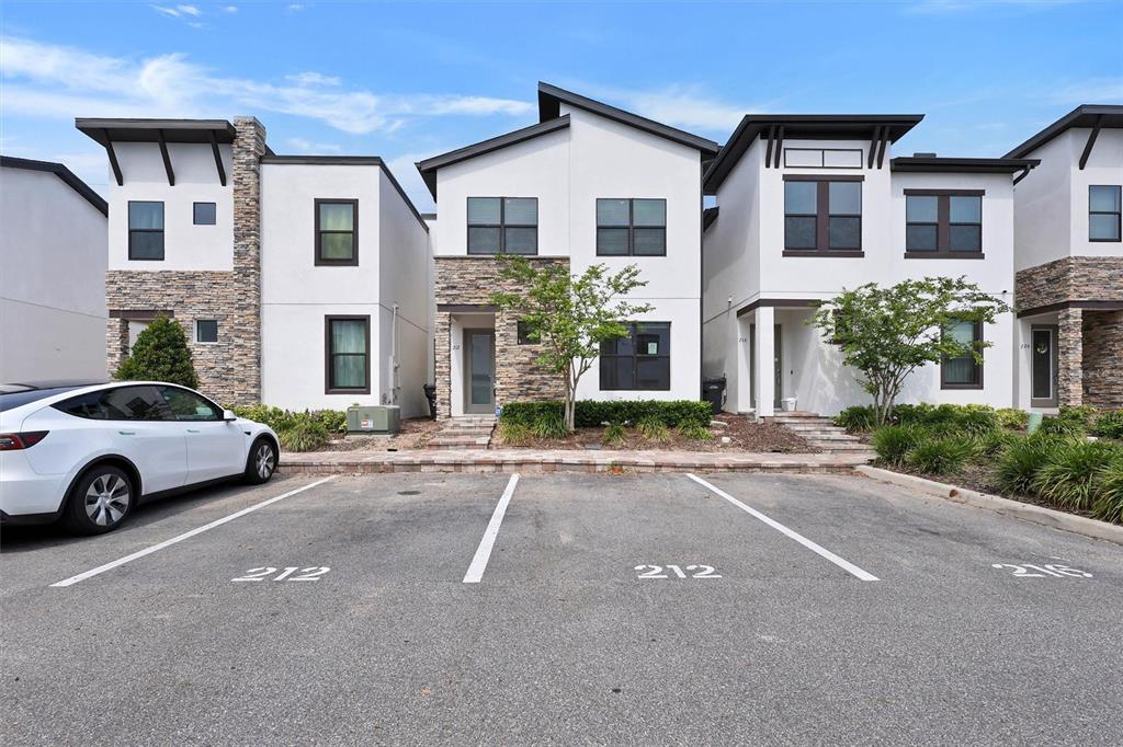 A row of modern townhomes with stone accents and white stucco exteriors faces a parking lot — 212 VILLA DOMANI CIRCLE, DAVENPORT, FL