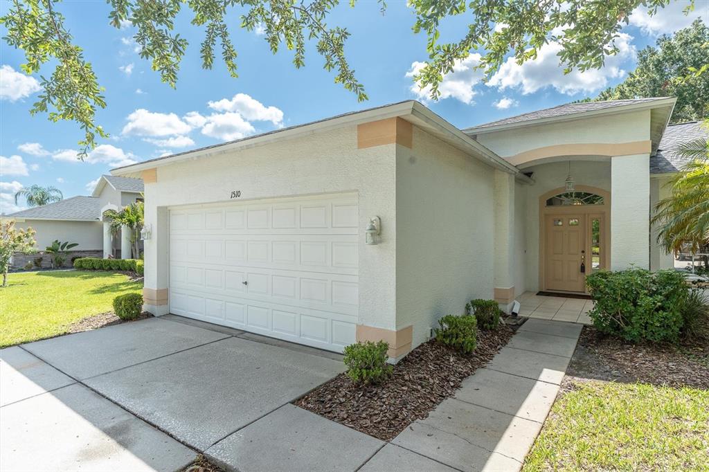 A single-story house exterior with a white stucco facade, a two-car garage, and a front entrance — 1510 MORNING ROSE PLACE, TRINITY, FL