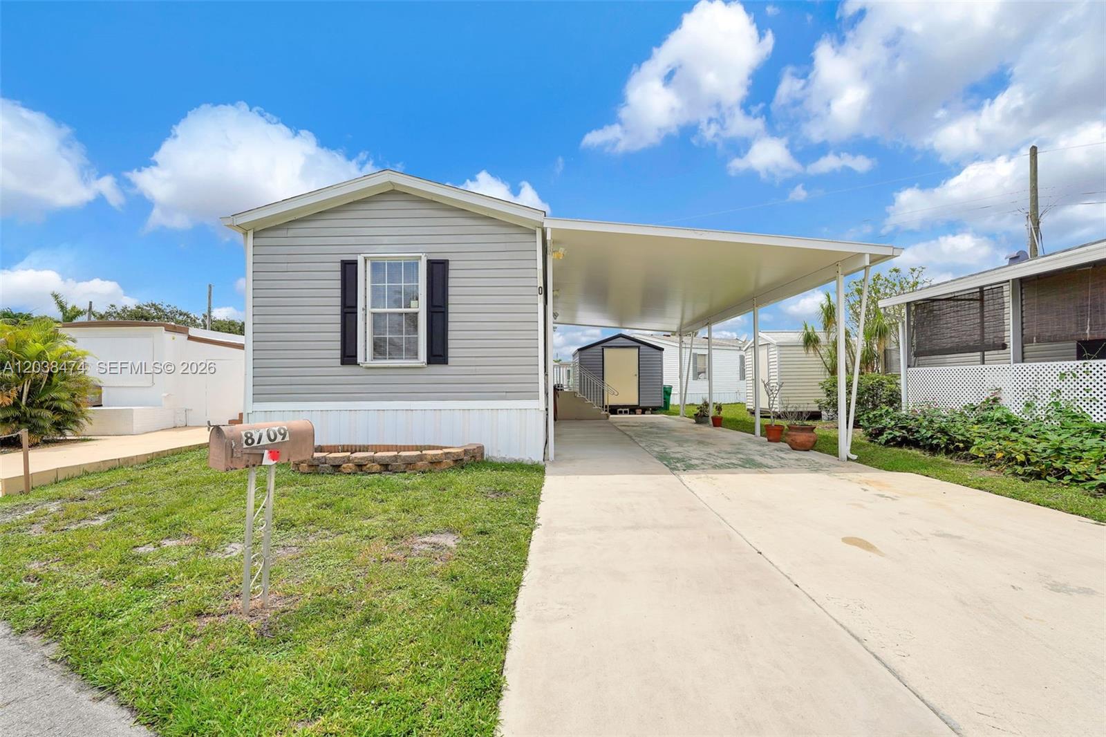 A light gray manufactured home features a concrete driveway, a carport, and a mailbox — 8709 SW 17th Ct, Davie FL 33324, DAVIE, FL