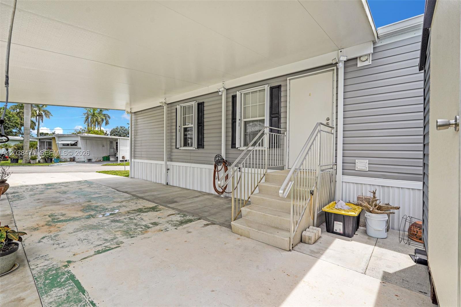 A gray mobile home features a covered carport, concrete steps, and a white entry door — 8709 SW 17th Ct, Davie FL 33324, DAVIE, FL