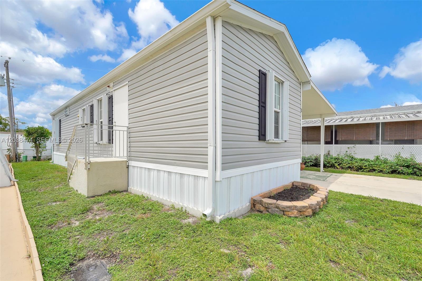 The exterior of a light gray manufactured home features white trim, shutters, and a concrete driveway — 8709 SW 17th Ct, Davie FL 33324, DAVIE, FL