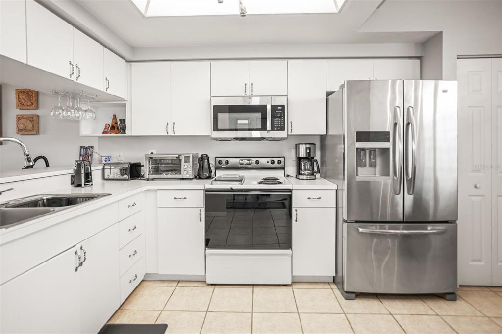 A kitchen with stainless steel appliances, white cabinets, and a small dining area by windows — 6399 SHORELINE DRIVE UNIT 4305, ST PETERSBURG, FL
