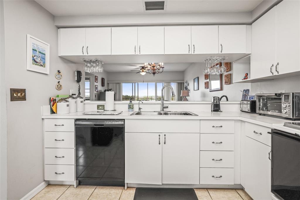 A kitchen with white cabinets, a black dishwasher, and a pass-through window to the living area — 6399 SHORELINE DRIVE UNIT 4305, ST PETERSBURG, FL
